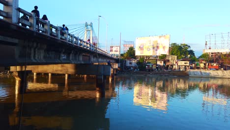 Bankerohan-Brücke,-Davao-Stadt,-Philippinen,-Mit-Einem-Mann-Beim-Angeln-Und-Menschen,-Die-Auf-Der-Brücke-Spazieren,-Sowie-Häusern-Und-Wasser