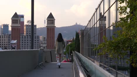 Mujer-Joven-Patinando-En-Un-Scooter-Eléctrico-Sobre-El-Puente-En-La-Plaza-De-España-En-La-Ciudad-De-Barcelona.