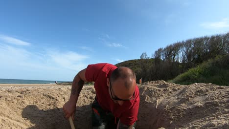 Ein-Mann-Gräbt-An-Einem-Sonnigen-Tag-Mit-Einer-Schaufel-In-Der-Grafschaft-Wicklow,-Irland,-Ein-Loch-In-Den-Strandsand-In-Brittas-Bay