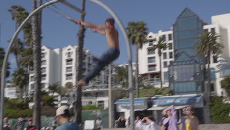 Un-Hombre-Balanceándose-En-Los-Anillos-De-Viaje-En-La-Playa-De-Santa-Monica-En-Los-Angeles-California