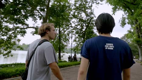 Male-Tourists-Walking-In-A-park-In-Hanoi,-Vietnam-With-Beautiful-Trees-and-Cloudy-Sky-Above---Wide-Shot