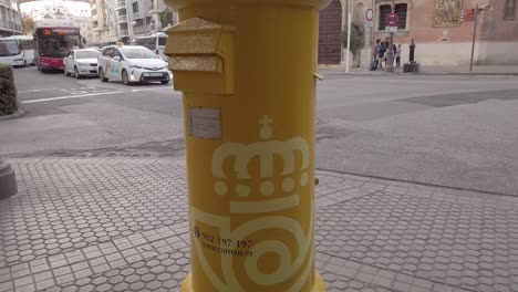 Inclinación-Hacia-Arriba-Del-Buzón-De-Correos-Amarillo-En-Sevilla,-España-Con-La-Iglesia-En-Segundo-Plano.