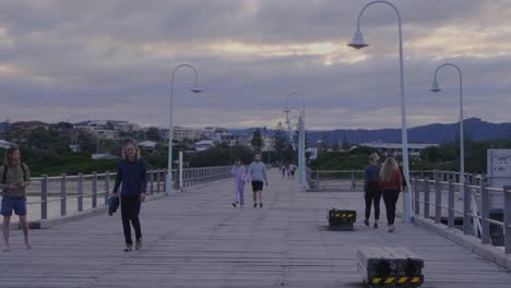 Menschen,-Die-Auf-Dem-Holzsteg-Spazieren---Sonnenuntergangsausflug-In-Coffs-Harbour,-New-South-Wales,-Australien---Gesamtaufnahme