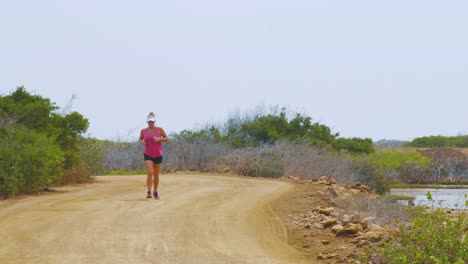 Eine-Aktive-Frau-Mit-Sonnenblende-Läuft-Auf-Der-Unbefestigten-Straße-In-Kralendijk,-Bonaire-–-Mittlere-Aufnahme