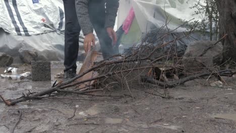 Young-kid-lighting-fire-in-Winter-bleak-wet-conditions-Moria-Refugee-Camp,-Mid-shot