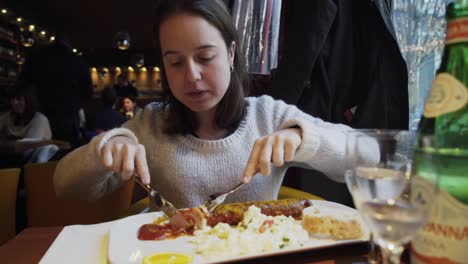 Mujer-Joven-En-El-Restaurante-Cortando-Una-Gran-Porción-De-Salchicha-Wurst-Alemana-En-Rodajas