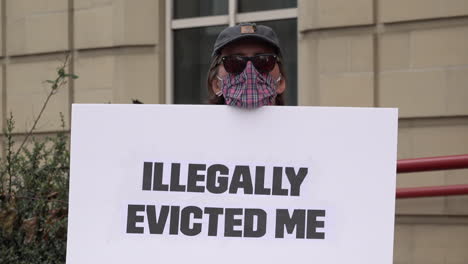 Ein-Demonstrant-Mit-Gesichtsmaske-Auf-Einer-Wohnungsbaudemonstration-Gegen-Die-Räumung-Während-Der-Coronavirus-Pandemie-Hält-Ein-Weißes-Pappschild-Mit-Der-Aufschrift-„Mich-Illegal-Vertrieben“-In-Der-Hand.