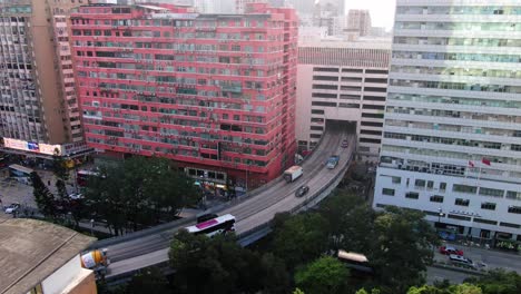 Traffic-passing-through-a-Car-park-building-in-downtown-Hong-Kong,-with-city-mega-buildings,-Aerial-view