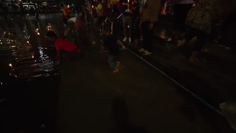 Thai-boy-haves-fun-in-the-City-Canals-water-when-other-people-in-masks-float-Loy-Krathongs-and-pray-at-night-during-Loi-Krathong-celebrations-in-Korat,-Thailand