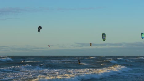 A-group-of-people-engaged-in-kitesurfing-in-sunny-autumn-day,-high-waves,-Baltic-Sea-Karosta-beach-in-Liepaja,-wide-shot