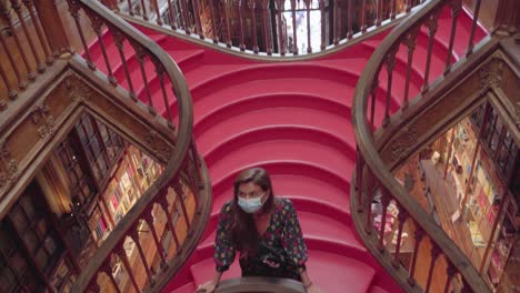 Una-Mujer-Se-Encuentra-En-Los-Escalones-De-Las-Escaleras-De-Caracol-De-La-Librería-Lello-En-Oporto,-Durante-La-Pandemia-De-Covid-19.