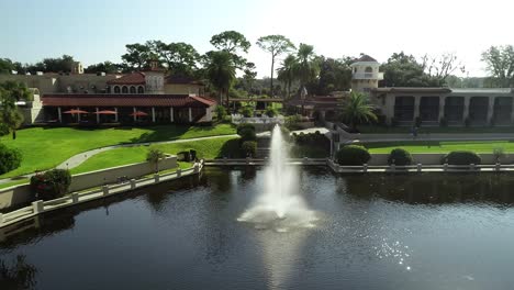 Luftaufnahme-Von-Stühlen,-Die-Für-Die-Hochzeitszeremonie-Mit-Blick-Auf-Einen-See-Mit-Springbrunnen-Im-Luxusresort-An-Einem-Sonnigen-Tag-In-Florida-Aufgestellt-Wurden