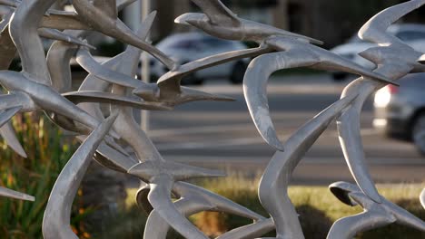 Escultura-De-Estatua-De-Pájaro-De-Metal,-Arte-De-La-Ciudad-Con-Coches-Circulando-En-Segundo-Plano.