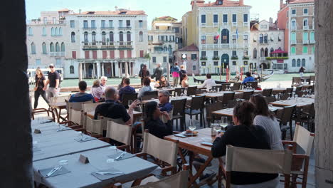 Dolly-forward-shot-of-tourist-enjoying-in-outdoor-restaurant-with-beautiful-backdrop-in-Venice,Italy