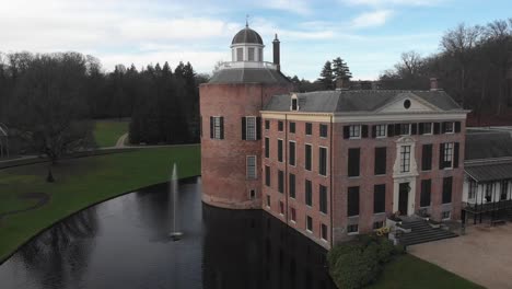 Slow-backward-aerial-distancing-of-Rosendael-castle-surrounded-by-design-garden-reflecting-in-the-still-water-of-the-moat-in-the-foreground