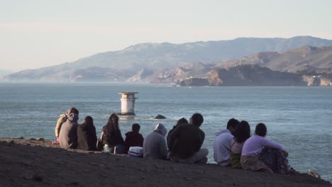 La-Familia-De-Turistas-Se-Relaja-En-El-Borde-De-La-Costa-Del-Pacífico-Durante-La-Puesta-De-Sol-En-El-Parque-Land&#39;s-End-De-San-Francisco