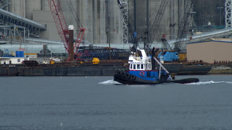 Fishing-Boat-Sailing-At-Burrard-Inlet-Passing-By-Industrial-Warehouse-With-Harbor-Cranes-In-Vancouver,-Canada