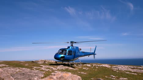 Privathubschrauber-Thront-Auf-Dem-Gipfel-Einer-Bergklippe-Mit-Blick-Auf-Die-Blaue-Meereslandschaft-Und-Der-Propeller-Dreht-Sich-Langsam-Nach-Links