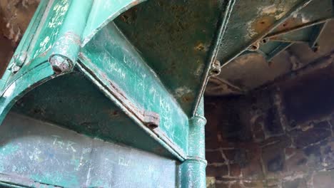 Crumbling-old-derelict-stonework-tower-with-fancy-wrought-iron-interior-staircase-looking-up-dolly-left