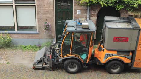 Steam-coming-out-of-weed-and-tares-pavement-clean-sweeper-machine-in-19th-century-cobble-stone-street