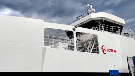 Ferry-Kinsarvik-from-Boreal-company-is-slowly-arriving-port-of-Kinsarvik-Norway---Static-closeupshot-of-ships-side-and-wheelhouse-with-company-logo-showing---Dark-moody-clouds-behind