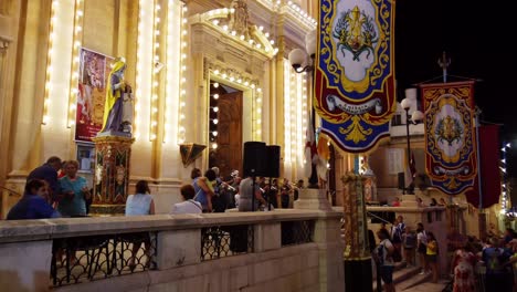 Malta,-Sliema,-local-religious-fiesta-with-crowd-facing-the-beautiful-and-decorated-church-and-orchestra-in-a-cozy-street-at-night