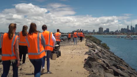 Toma-En-Cámara-Lenta-De-Voluntarios-Limpiando-La-Playa-Y-La-Costa-En-Australia-Con-El-Horizonte-De-Melbourne-Al-Fondo