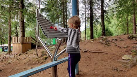 Junges-Blondes-Mädchen-Spielt-Draußen-Xylophon-Im-Vergnügungspark-Mikkelparken-In-Norwegen---Andere-Menschen-Gehen-Im-Hintergrund-Vorbei