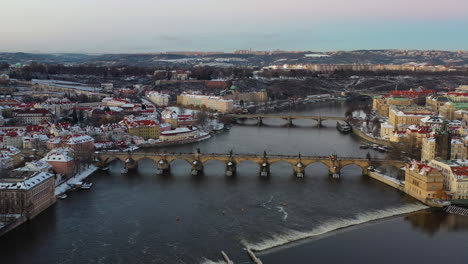 Vista-Aérea-De-Karluv-Most-Y-El-Paisaje-Urbano-De-Praga-En-Una-Noche-De-Invierno,-Edificios-Nevados-Y-El-Río-Vltava,-República-Checa