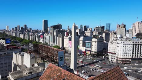 Drone-flying-over-chalet-house-on-top-of-terrace-of-a-nine-story-building-,-from-monumental-Obelisco-at-republic-square-during-daytime-with-busy-rush-hours-traffic-travelling-on-9-de-Julio-avenue