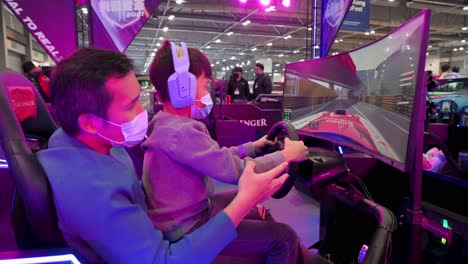 Padre-E-Hijo-Juegan-Videojuegos-De-Carreras-Temáticos-Durante-La-Expo-Internacional-Del-Motor-Que-Exhibe-Autos-Y-Motocicletas-Térmicos-Y-Eléctricos-En-Hong-Kong