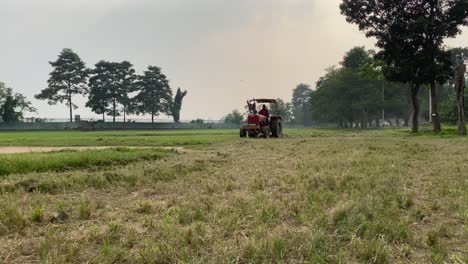 Vista-Frontal-De-Un-Granjero-En-Un-Tractor-Rojo-Arando-El-Campo-Verde-Para-Hacer-Un-Campo-De-Golf