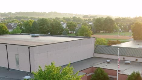 Sobrevuela-El-Techo-De-La-Escuela-Primaria-Doe-Run,-Revelando-Un-Patio-Vacío-En-El-Fondo-A-La-Luz-Del-Sol-Dorado-De-La-Mañana