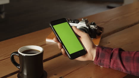 Zoom-in-shot-of-male-Photographer-drinking-coffee-and-looking-at-maps-for-nice-spots-on-Mobile-Phone---Green-Screen-background