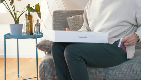 Person-sitting-on-couch-unwrapping-new-M1-MacBook-Pro-box,-peeling-off-plastic