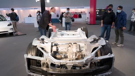 Los-Visitantes-Miran-Y-Toman-Fotos-De-Un-Automóvil-Con-Chasis-De-Motor-Tesla-Y-El-Bastidor-De-Un-Vehículo-De-Motor,-Durante-La-Exposición-Internacional-Del-Motor-Que-Muestra-Automóviles-Eléctricos-Ev-En-Hong-Kong