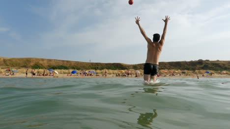 Punto-De-Vista-De-ángulo-Bajo-En-Cámara-Lenta-Del-Portero-Tratando-De-Salvar-La-Pelota-Pateada-Desde-La-Playa-Saltando-En-Agua-De-Mar,-Punta-Penna-En-Italia