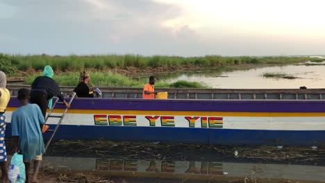 African-people-boarding-a-big-wooden-boat-at-sunset,-Salaga