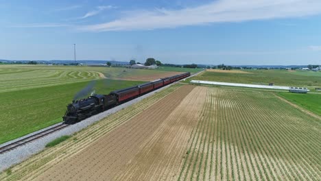 Eine-Luftfahrt-Mit-Blick-Auf-Eine-Dampfmaschine,-Die-Rauch-Und-Dampf-Ausstößt,-Mit-Reisezugwagen,-Die-Auf-Einer-Eingleisigen-Strecke-Durch-Fruchtbares-Ackerland-Und-Eine-Landschaft-Fahren,-Mit-Einem-Bauern,-Der-Im-Hintergrund-Arbeitet