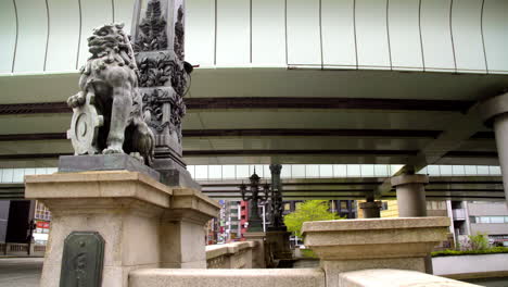 Tokio,-Japón,-Alrededor-De-Abril-De-2020:-Peatones-Caminando-Por-El-Histórico-Puente-Nihonbashi,-León-Tallado-En-Piedra-Sentado-En-El-Borde,-En-La-Antigua-Zona-Financiera-Del-Centro-De-La-Ciudad-En-El-Barrio-Urbano-Central,-Noche