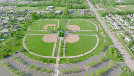 Tagesluftaufnahme-über-Baseball-Diamanten-Und-Grünen-Feldern,-Häusern,-Straße-Und-Parkplatz-Darunter