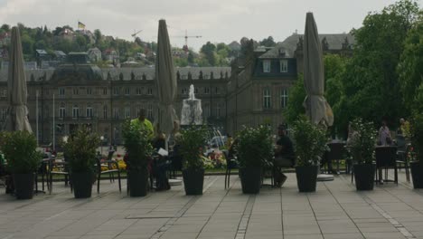 Turista-Caminando-Por-La-Gente-Comiendo-En-La-Acera-En-El-Centro-De-La-Plaza-De-Stuttgart-Al-Mediodía,-Alemania,-Europa,-ángulo-De-Visión-Panorámica