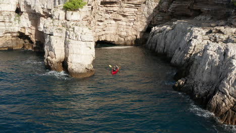 Aerial-View-Of-Tourists-Kayaking-Near-Cliffs-And-Caves-In-Pula,-Istria,-Croatia---drone-shot