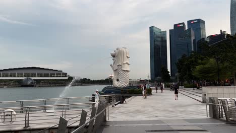 Los-Turistas-Que-Visitan-Y-Los-Lugareños-Hacen-Ejercicio-En-El-Parque-Merlion-En-El-área-Metropolitana-Del-Centro-Con-Edificios-Comerciales-Y-Financieros-En-El-Fondo