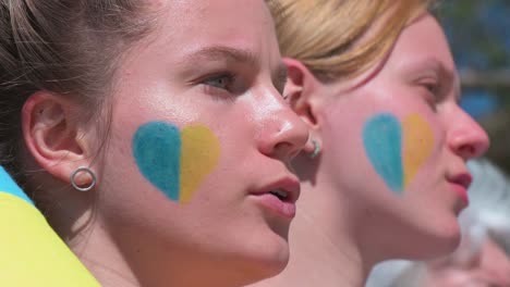 Los-Manifestantes-Son-Vistos-Con-Sus-Rostros-Pintados-Con-Forma-De-Corazón-En-Colores-Azul-Y-Amarillo,-Los-Colores-De-La-Bandera-De-Ucrania,-Durante-Una-Manifestación-Contra-La-Invasión-Rusa-De-Ucrania-En-España