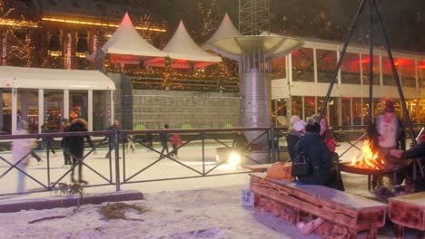 Mucha-Gente-Patinando-En-Una-Colorida-Pista-De-Patinaje-Sobre-Hielo-Por-La-Noche-Calentándose-Junto-A-Una-Fogata-Durante-El-Invierno-En-Oslo,-Noruega