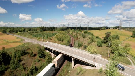 Freight-Train-Carrying-Vital-COVID-supplies-Crossing-the-Country-under-road-bridge-through-green-landscape-with-bright-blue-sky-on-a-clear-day