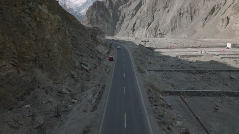 Car-Driving-Along-Highway-Into-Horizon-In-Hunza-Valley-With-Tilt-Up-View-Of-Snow-Capped-Mountains-In-Distant-Background