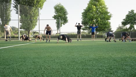 Many-of-men-in-sportswear-gathered-on-a-soccer-field-doing-burpies