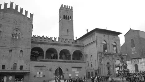 Fotografía-En-Blanco-Y-Negro-De-Los-Turistas-Que-Se-Aglomeran-Alrededor-Del-Palazzo-Del-Podesta-En-Bolonia,-Italia-Durante-El-Día.